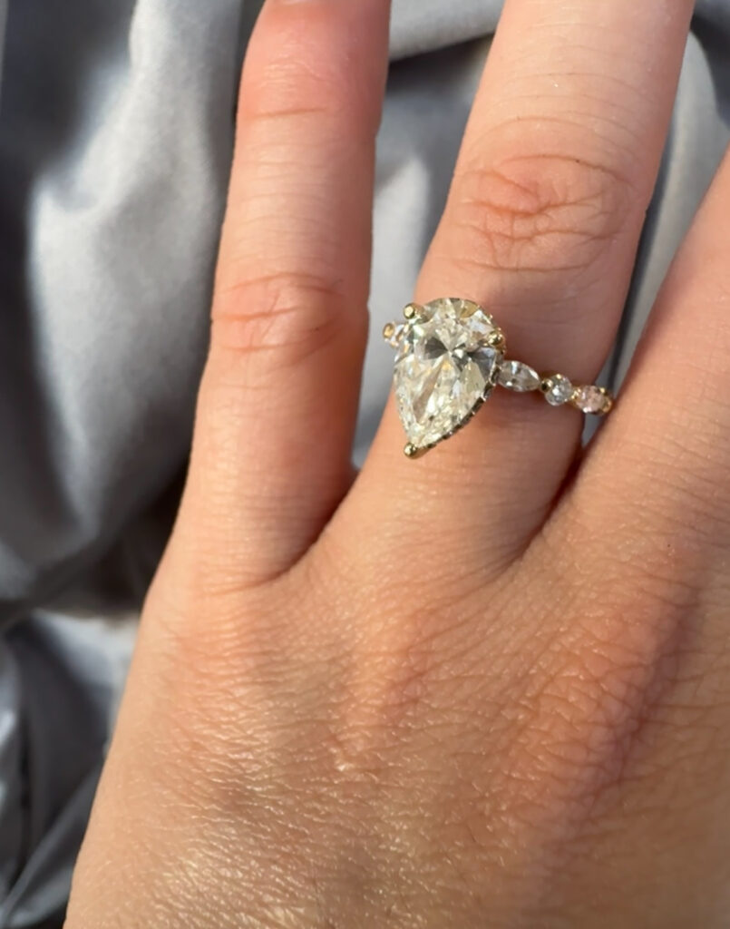 pear shaped custom diamond ring with marquise and round diamonds band in a finger